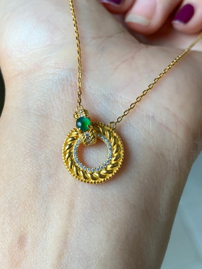 May include: A gold necklace with a circular pendant featuring a green gemstone and small clear stones around the edge.