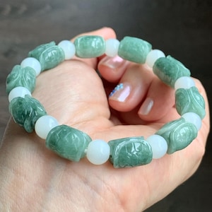 May include: A jade bracelet featuring alternating green turtle-shaped beads and white round beads. The turtle beads have carved details. The bracelet is strung on an elastic band. The bracelet is a piece of jewelry.