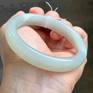 Puede incluir: Una taza de cerámica blanca con un asa negra y el texto "But First, Coffee" en un estilo manuscrito. La taza está sobre una superficie blanca. La taza mide aproximadamente 10 cm de alto.