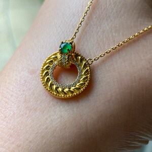May include: A gold necklace with a circular pendant featuring a green gemstone and a row of clear stones around the edge.
