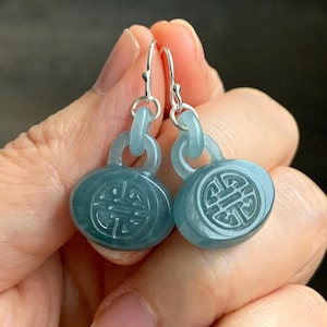 May include: A pair of silver dangle earrings with blue jade oval charms featuring a carved Chinese knot design.