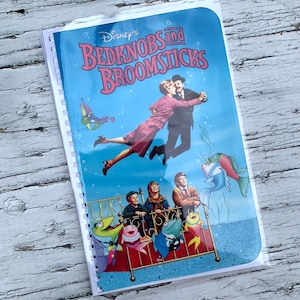 May include: A blue and white book cover with the title "Disney's Bedknobs and Broomsticks" in red and white lettering. The cover features a couple dancing underwater with a bed and fish in the background.