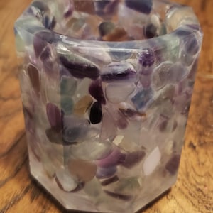May include: A clear glass candle holder with a hexagonal shape filled with small, colorful, iridescent stones.