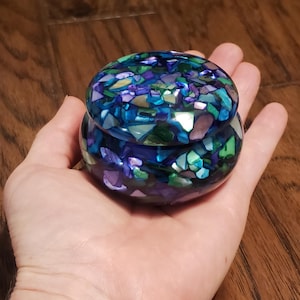 May include: A small, round, blue and green trinket box with a mosaic design. The box is made of resin and has a lid.