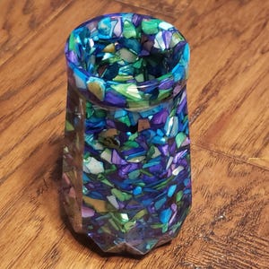 May include: A small, clear glass vase with a geometric shape. The vase is filled with colorful, mosaic-like pieces of glass in shades of blue, green, purple, and white.