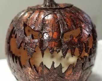 Puede incluir: Una escultura de calabaza de color marrón oscuro con textura y una expresión facial tallada, dentada y amenazante. La superficie tiene un aspecto rústico y desgastado con grietas profundas y un tallo en la parte superior, revelando un interior hueco.