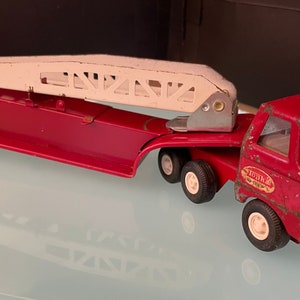 May include: A red toy fire truck with a white ladder and a "Tonka" logo on the side. The truck has a clear plastic windshield and a detailed front grill.