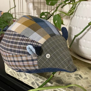 May include: A patchwork fabric hedgehog toy with blue, brown, and green plaid patterns. The toy has a button eye and is sitting on a tray with a green plant.