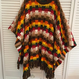 May include: A colorful crocheted poncho with a striped pattern in shades of brown, orange, yellow, red, and white. The poncho has fringe along the bottom edge.
