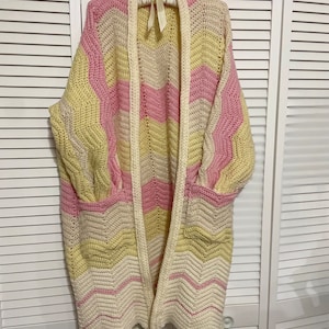May include: A long, crocheted cardigan with a chevron pattern in pink, yellow, and white.
