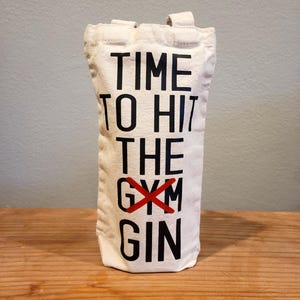 May include: White canvas tote bag with black text that reads "TIME TO HIT THE GYM GIN" with a red X over the word "GYM".