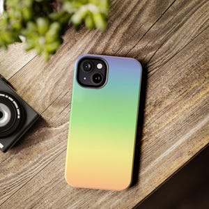 May include: A smartphone case with a gradient design. The case transitions from blue at the top to green in the middle and yellow at the bottom. The phone case is on a wooden surface.