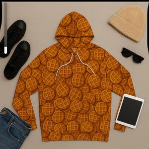 May include: A brown waffle-patterned hoodie with a white drawstring, black sneakers, a tan beanie, black sunglasses, a tablet, and blue jeans. The hoodie is the focal point, covered in a repeating waffle design.