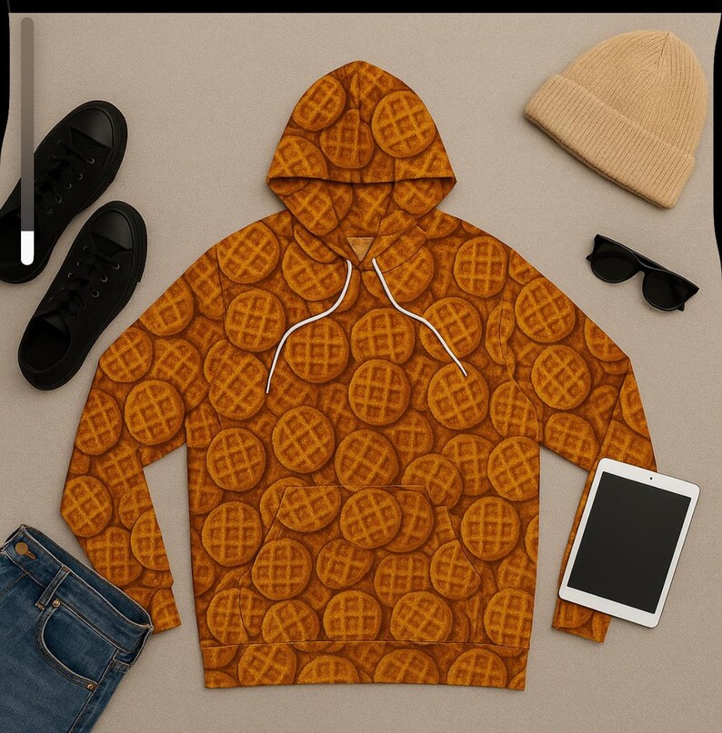 May include: A brown waffle-patterned hoodie with a white drawstring, black sneakers, a tan beanie, black sunglasses, a tablet, and blue jeans. The hoodie is the focal point, covered in a repeating waffle design.