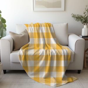 May include: A yellow and white plaid throw blanket on a white sofa. The blanket has a checkered pattern with a yellow background and white squares.