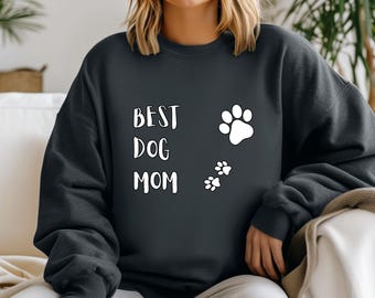 Puede incluir: Una sudadera gris oscuro con el texto "BEST DOG MOM" en letras blancas y huellas de patas blancas.