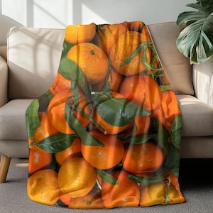 May include: A soft orange and green throw blanket with a pattern of oranges. The blanket is made of a soft, plush material and is perfect for cuddling up on the couch.