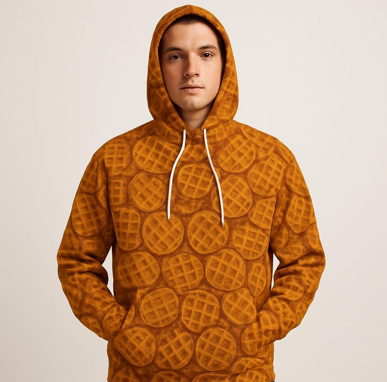 May include: A hooded sweatshirt featuring a repeating pattern of waffles in shades of brown. The hoodie has a drawstring and a front pocket. The waffle design covers the entire garment, including the hood. The overall style is casual and comfortable.