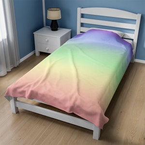 May include: A single bed with a white frame and a rainbow ombre comforter. The comforter is a gradient of pink, yellow, green, blue, and purple.