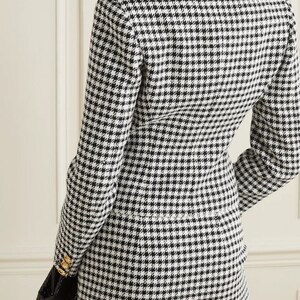 Może przedstawiać: Czarno-biała sukienka typu blazer w kratę typu &bdquo;pieski&rdquo; z złotymi guzikami. Sukienka ma dopasowany kr&oacute;j i długie rękawy.
