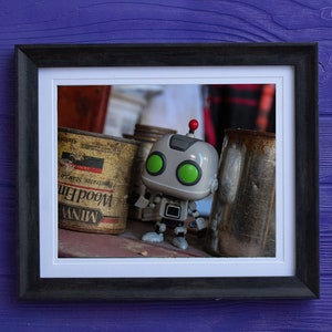 Peut inclure: Un petit robot jouet gris avec des yeux verts et une antenne rouge se tient sur une surface en bois à côté de trois boîtes en métal vintage. Les boîtes sont étiquetées "Miniw" et "Woodlife" avec une apparence délavée et jaunâtre.