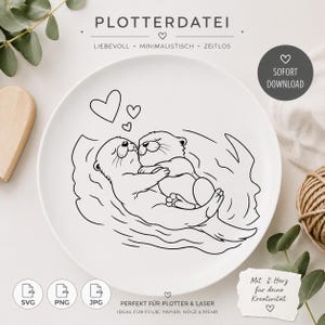 Op de afbeelding: Een witte keramische plaat met een zwarte lijntekening van twee otters die elkaar omhelzen, met drie harten erboven. De plaat heeft tekst, waaronder "PLOTTERDATEI" en "PERFEKT FÜR PLOTTER & LASER".