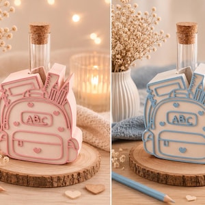 May include: A white desk organizer shaped like a backpack with a glass test tube vase. The backpack features raised outlines in either pink or blue, with the letters ABC on the front pocket, heart accents, and molded school supply details.