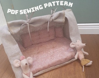 May include: PDF sewing pattern for a dollhouse sofa with a linen canopy. The sofa is pink and white with a tufted back and a pink and white striped mattress. Two small mouse dolls are sitting near the sofa.