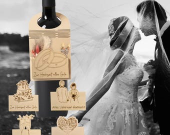 May include: A black wine bottle with a wooden tag featuring laser-cut wedding-themed designs and text. The tag includes images of wedding rings, a cake, champagne glasses, and a heart-shaped tree. The text reads "Zur Hochzeit alles Gute" and "Alles Liebe zur Hochzeit."