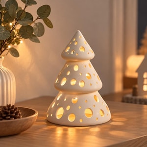 May include: A white ceramic Christmas tree-shaped candle holder featuring a tiered design with numerous circular cutouts of varying sizes. The structure is hollow, allowing warm light to emit from within, casting soft circular patterns on the surface.
