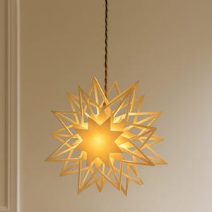 May include: A star-shaped pendant light fixture with a warm, inviting glow. The light is suspended from a brown cord and features a layered design of interlocking star shapes. The fixture casts a soft, ambient light, perfect for adding a touch of elegance to any room.