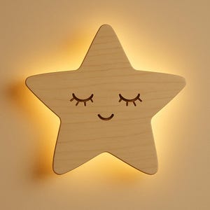 Op de afbeelding: Houten ster-vormige wandlamp met een lachend gezicht en gesloten ogen. Het licht heeft een warme gloed en de ster is gemaakt van lichtgekleurd hout. Het ontwerp is eenvoudig en geschikt voor een kinderkamer.