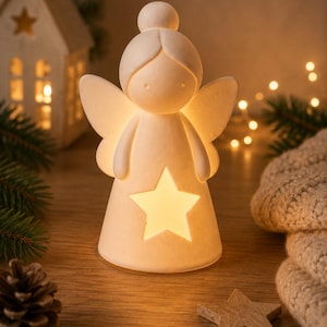 May include: A matte white ceramic angel figurine with a smooth, rounded head and stylized wings. The body of the angel features a central star-shaped cutout that emits a warm, soft glow from an internal light source, creating a bright illumination.