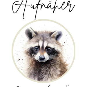 Op de afbeelding: Waterverfillustratie van een wasbeer in een beige cirkel, met het woord "Aufnäher" erboven. Daaronder pictogrammen van een schaar, een strijkijzer en een naald met draad. De wasbeer heeft bruine en grijze vacht en een zwart masker.