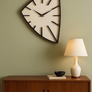 May include: A modern, triangular wall clock with a cream-colored face and black hands and markers hangs above a wooden cabinet. A white lamp with a beige shade and a small black bowl sit on the cabinet.