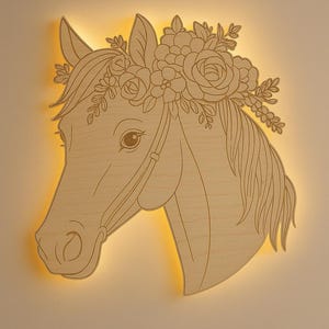 May include: Wooden horse head wall art with a floral crown. The horse is in profile, with detailed lines and a warm, natural wood finish. The piece has a soft, glowing light emanating from behind the wood.