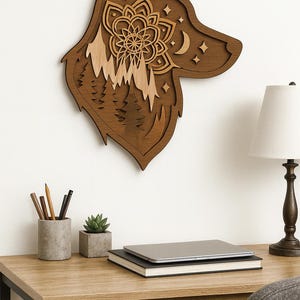 Puede incluir: Arte de pared de madera con forma de cabeza de lobo. El diseño presenta una escena de montaña en capas, un mandala floral, estrellas y una luna creciente. La obra de arte está hecha de madera marrón y clara.