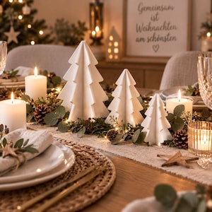 Peut inclure: Un centre de table composé de trois figurines de sapins de Noël géométriques et blanches, disposées sur un chemin de table avec des feuilles d'eucalyptus, des pommes de pin et des bougies piliers blanches allumées, près de couverts et verres.