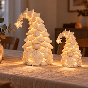 May include: Two cream-colored gnome figurines with textured, layered hats that curve downward, each topped with a glowing star. The figures feature rounded noses, bushy beards, and internal warm lighting that illuminates the carved details.