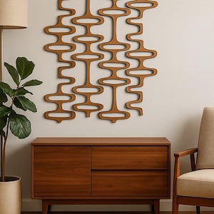 May include: A mid-century modern wooden wall art piece with an abstract design of interconnected shapes. Below, a matching wooden cabinet with two drawers and a door. A beige armchair and a potted plant complete the room's decor.