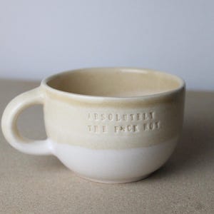 Könnte beinhalten: Eine weiße Keramiktasse mit beigefarbenem Rand und dem Aufdruck "ABSOLUTELY THE F*CK HOT."