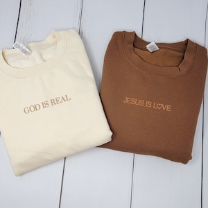 May include: Two sweatshirts, one cream colored with the text "GOD IS REAL" and one brown with the text "JESUS IS LOVE".