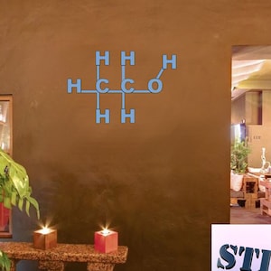 May include: A blue chemical formula for a molecule is displayed on a brown wall. The formula is for a molecule with two carbon atoms, four hydrogen atoms, and one oxygen atom. The formula is displayed in a modern, minimalist style. The wall is in a room with a wooden floor and a doorway leading to another room. The doorway is framed by a brown wall. The room is decorated with a plant in a pot and two candles on a table.