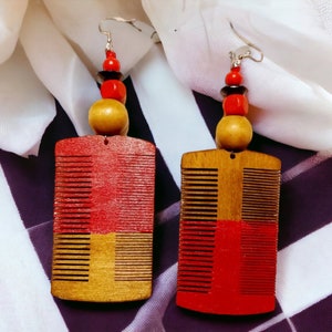 May include: A pair of wooden earrings with red and brown comb-shaped pendants. Each earring features a stack of red and black beads.