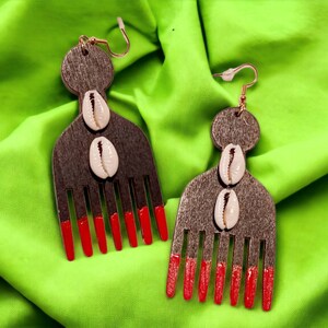 May include: A pair of wooden earrings shaped like an afro pick with red tips and white cowrie shells.