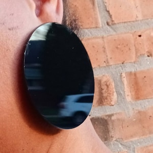 May include: A large, round, black earring with a reflective surface.