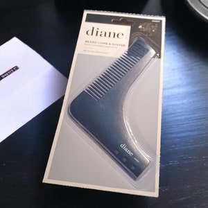 May include: A black plastic beard comb and shaper with the text "Diane" on the packaging. The comb is shaped like a curved line with teeth on one side.