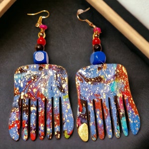 May include: A pair of blue and gold earrings with a comb-like design. The earrings are made of wood and have a blue, red, and black bead accent.
