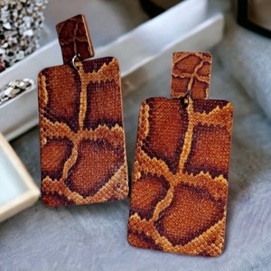 May include: A pair of brown and tan rectangular dangle earrings with a snake skin pattern.