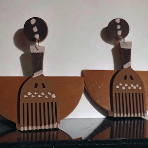 May include: A pair of wooden earrings with a brown and white comb design. The earrings are shaped like a half-circle and have a small brown circle at the top.